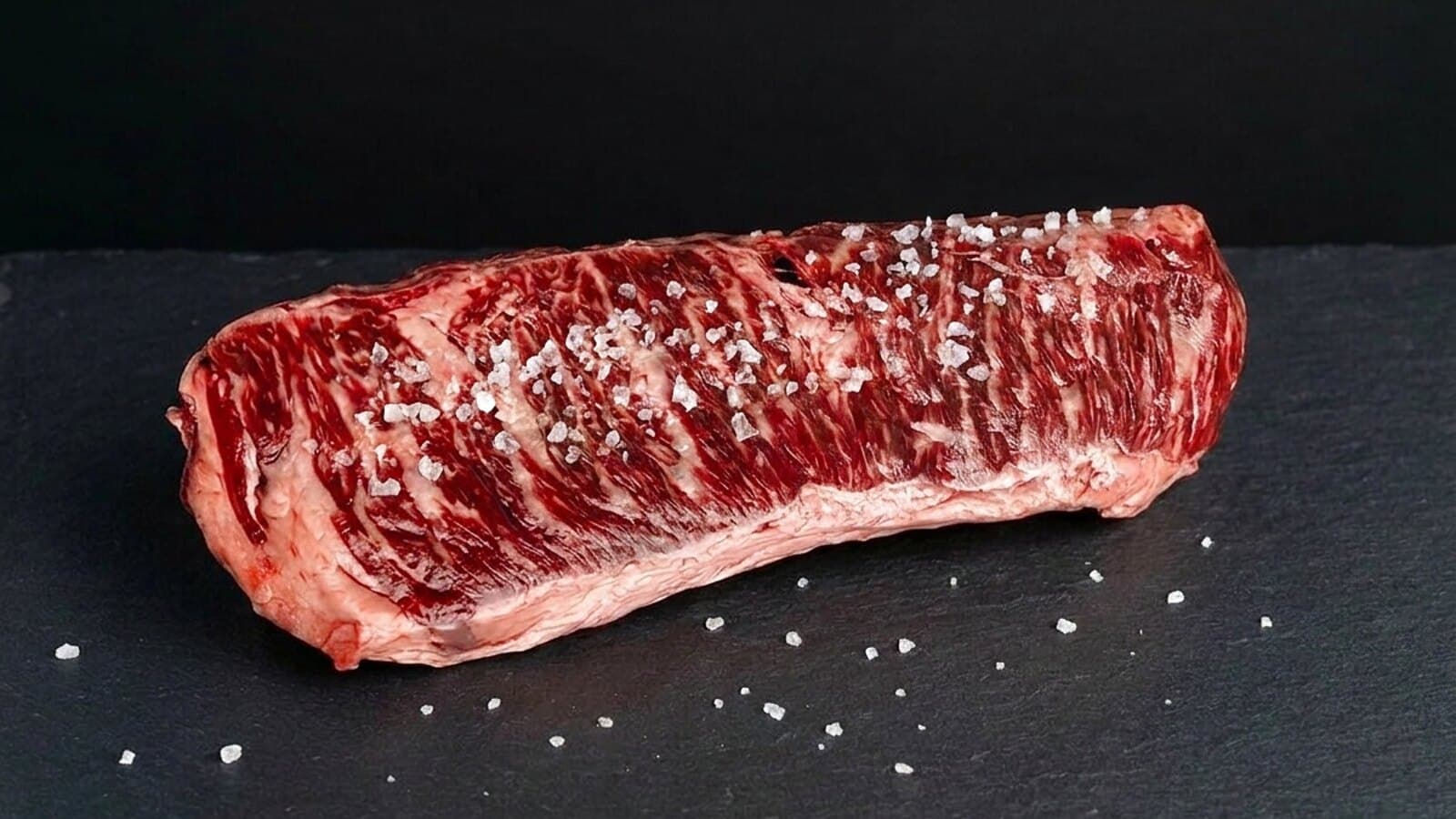 Grobes Meersalz auf einem rohen Skirt Steak auf dunklem Schiefer