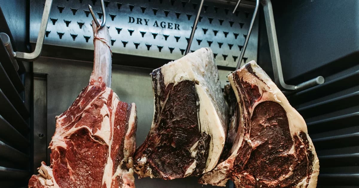 Drei Rib-Eye-Stücke am Haken im Reifeschrank — frisch neben 28 Tage trocken gereift