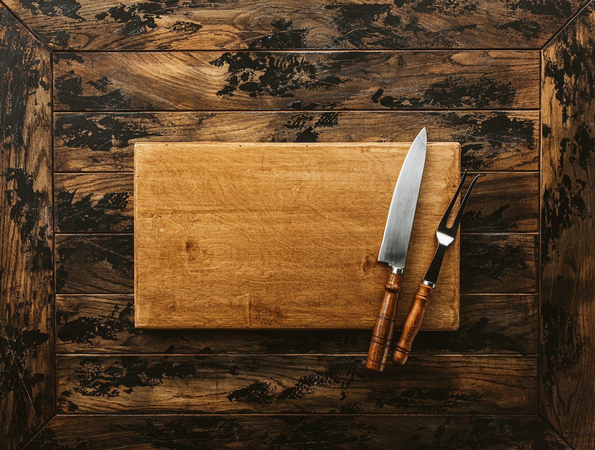 Zwei Messer auf einem hellen Holzschneidebrett vor dunklem Holzuntergrund