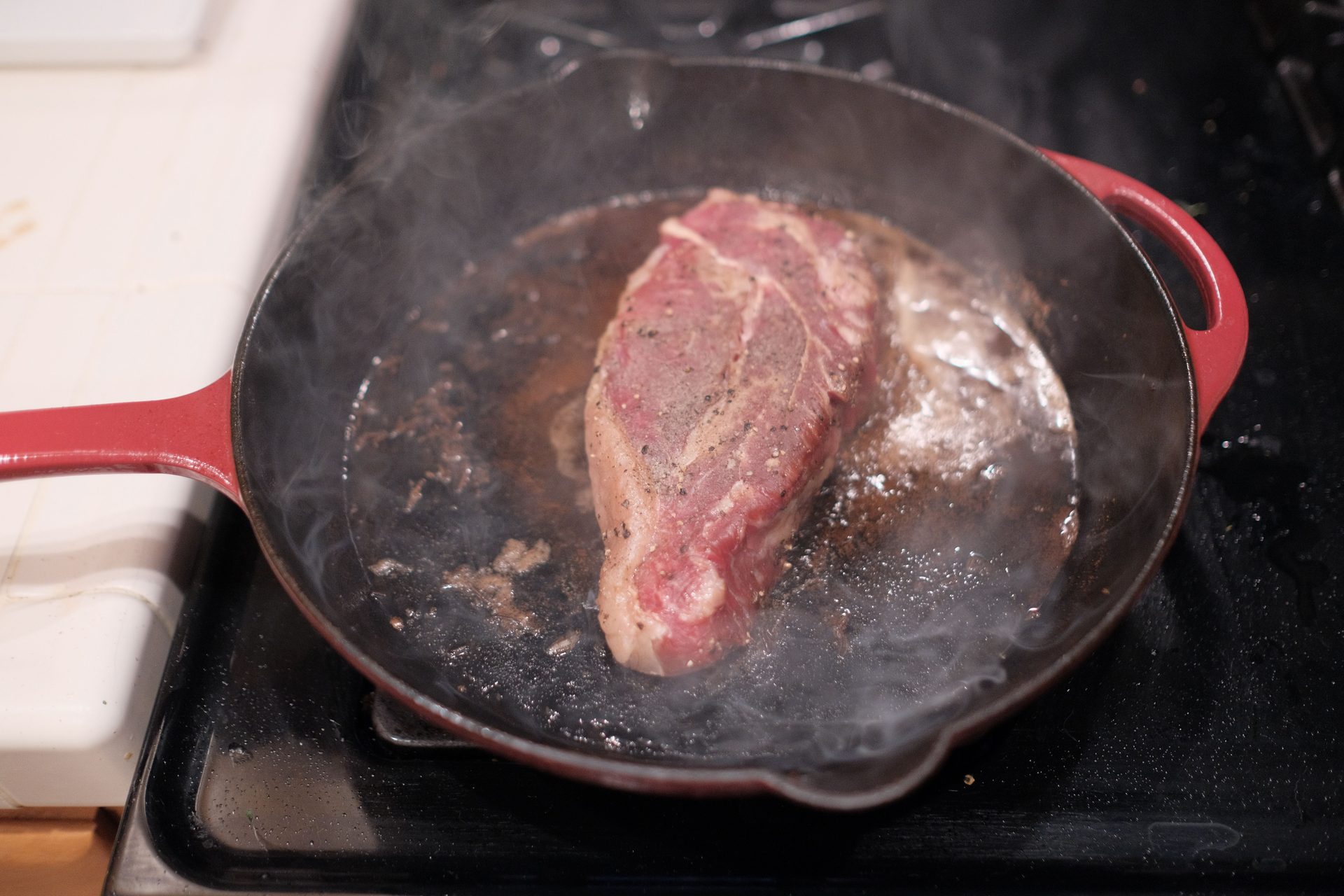 Steak in heißer Gusseisenpfanne, Dampf steigt über der bräunenden Oberfläche auf